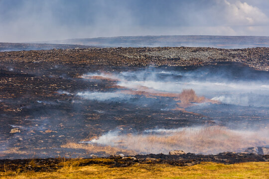 Smoke rising from burnt ground after wildfire on Llangynidr Moors, Brecon Beacons, charred earth and scorched vegetation across upland landscape