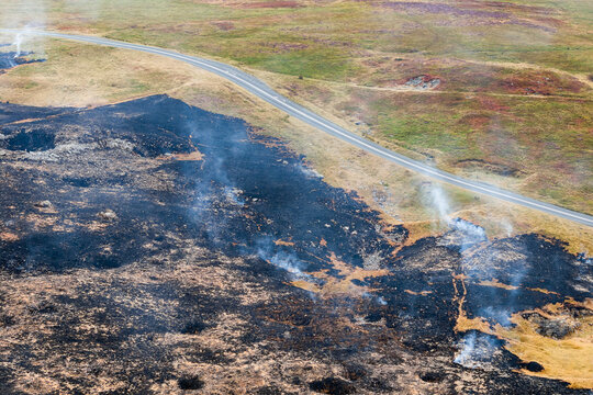 Charred earth and smoldering smoke plumes following wildfire on Llangynidr Moors, Brecon Beacons National Park, Wales, high angle view