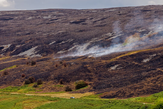 Smoke rising from charred hillside after wildfire on Llangynidr Moors, Brecon Beacons, blackened moorland sloping down to green bracken in South Wales