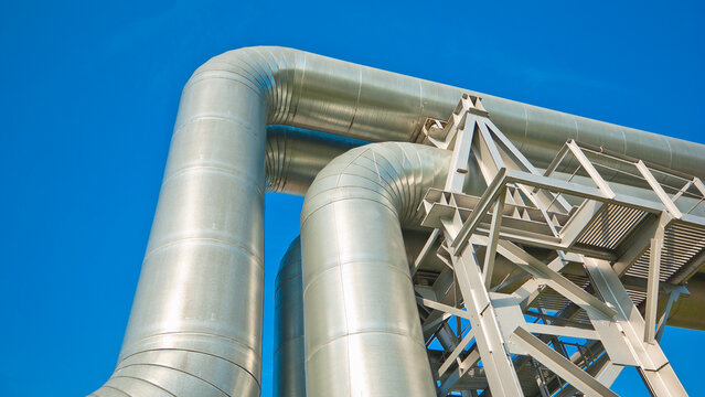 The photo shows a close-up of a straight pipeline on a metal support against a blue sky