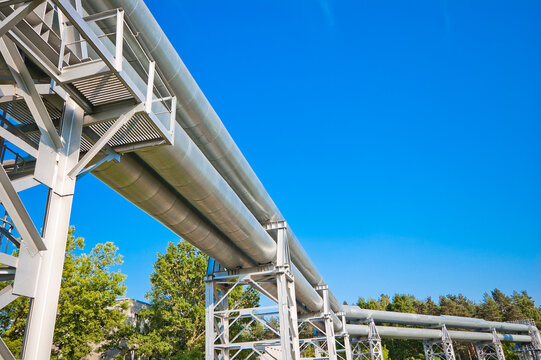 The photo shows a pipeline on metal supports against a blue sky