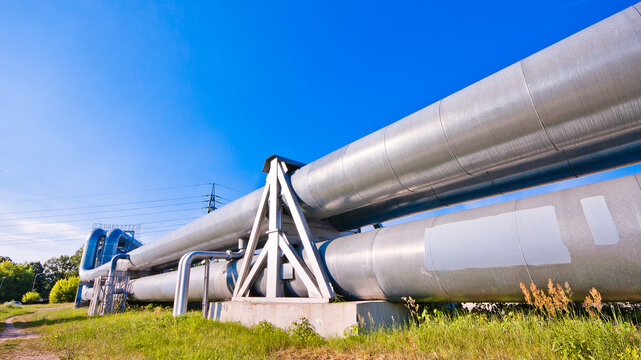 A close-up of a pipeline, with a blue sky and a power transmission tower in the background