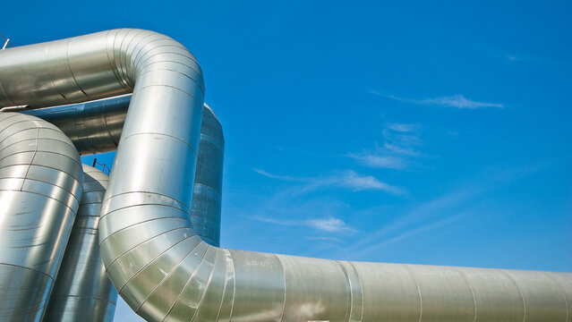 The photo shows a curved pipeline and a power transmission tower against a blue sky