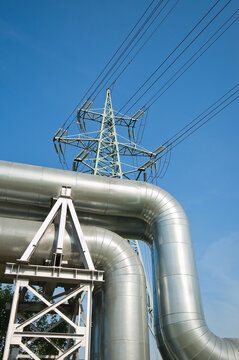 The photo shows a pipeline and a power transmission tower against a blue sky