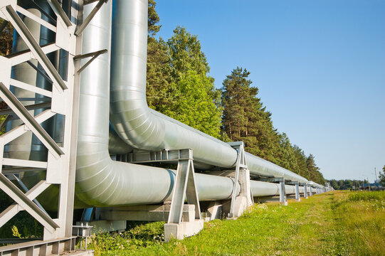 The photograph shows a pipeline against a backdrop of blue sky and green forest