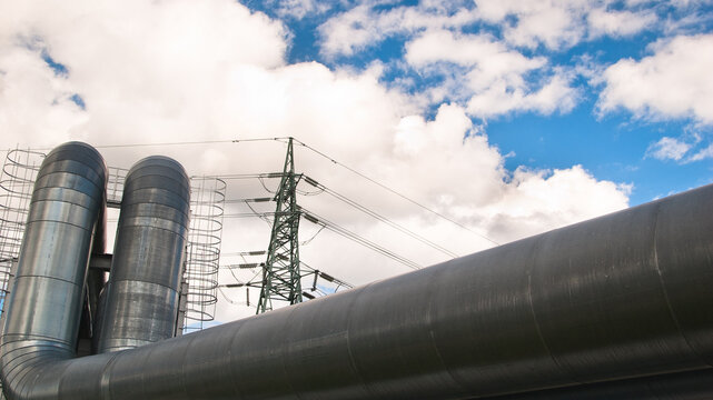 a pipeline and a power transmission tower against a blue sky and clouds