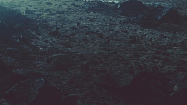 The scene shows a rocky surface on an alien planet. The ground is uneven with many stones, and the lighting is dim. There are distant shadows and a sense of vast emptiness.
