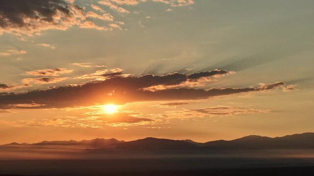 Aerial view of a golden sun rising through a cloud layer above the Rocky Mountains with wildfire smoke haze in the atmosphere in Santa Fe, New Mexico, United States.