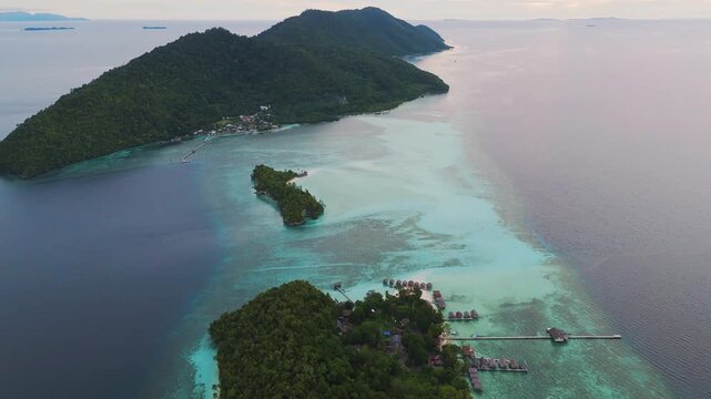Aerial view of Mios Kri island with lush tropical vegetation, turquoise waters, and overwater bungalows in West Supiori, Papua, Indonesia.