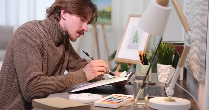 Man painting picture at wooden desk indoors. Artist working in studio