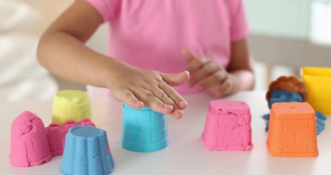 Little girl playing with colorful kinetic sand at white table indoors, closeup
