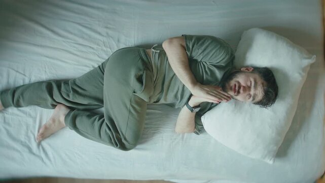 Man lying in bed praying with folded hands before falling asleep, top view