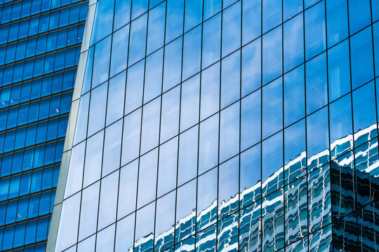 Modern blue glass building facade with geometric window patterns and abstract reflections, creating a sleek urban architecture background for business, technology, finance, and design concepts.