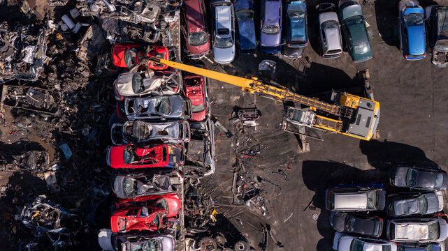 Aerial view of a yellow crane lifting a car in a scrapyard filled with crushed vehicles and automotive parts in Gdansk, Poland.