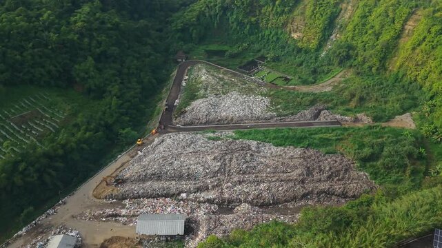 Aerial view of TPA Bangli landfill site with heavy machinery and surrounding lush green hills in Bangli, Bali, Indonesia.