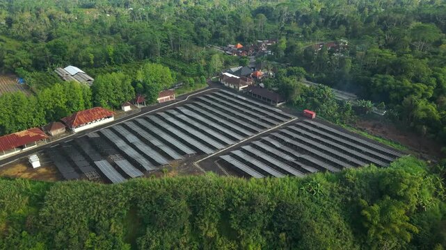 Aerial view of PLTS 1MWp Bangli solar power plant surrounded by lush tropical greenery and trees in Bangli, Bali, Indonesia.