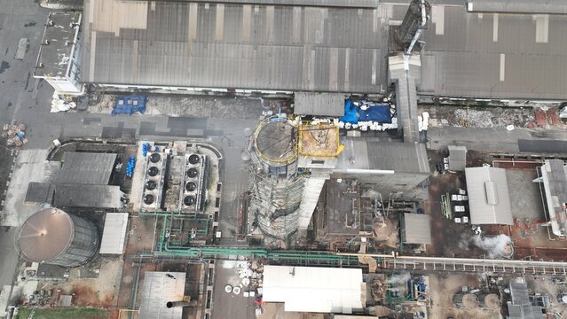 Aerial view of an industrial facility featuring a central tower, cooling units, storage tanks, and factory buildings with pipes and steam vents in Cikampek, West Java, Indonesia.