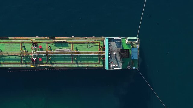 Aerial view of a large industrial tanker ship with a green deck floating on deep blue sea water in Buleleng, Bali, Indonesia.