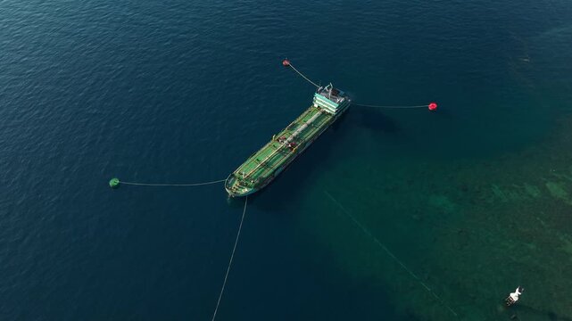 Aerial view of a tanker ship anchored in the calm blue sea with mooring buoys in Buleleng, Bali, Indonesia.