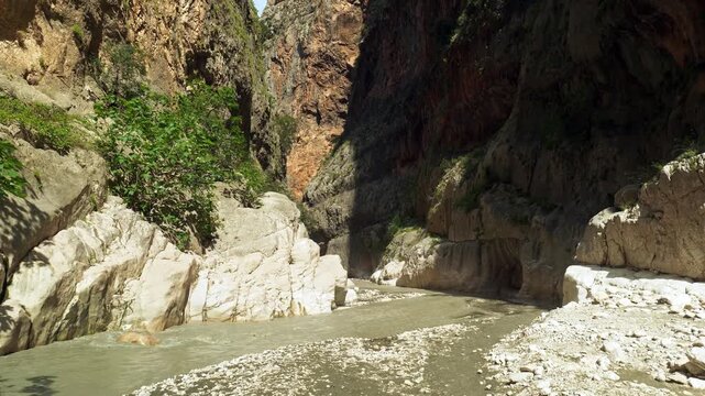 Narrow gorge with river flowing through rugged rock formations under bright sunlight.