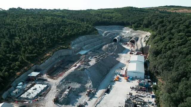 Aerial view of a tunnel construction site featuring heavy machinery, excavation piles, and temporary buildings surrounded by dense forest in Istanbul, Istanbul, Turkiye.