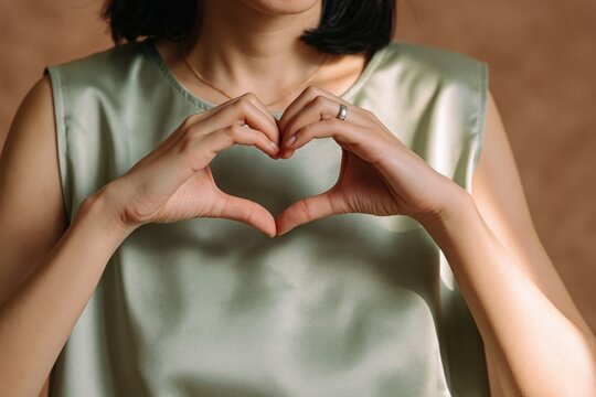 Woman making a heart shape with her hands to show love and kindness as a gesture