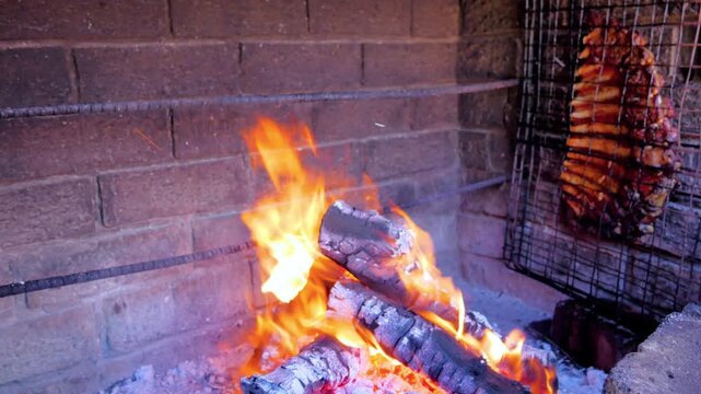 Grilled pork ribs roasting over open wood fire flames inside rustic brick barbecue pit for traditional outdoor cooking.