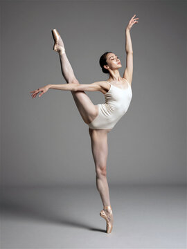 Professional ballerina in white leotard performing vertical leg extension split in studio