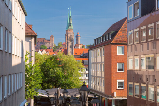 View across Nuremberg, Germany, with a historic church tower, red rooftops and medieval towers under a clear blue sky.