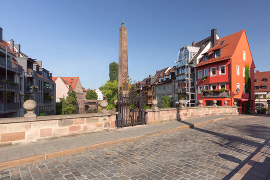 Stone monument beside the Pegnitz River surrounded by traditional buildings and cobblestone streets in Nuremberg, Germany.