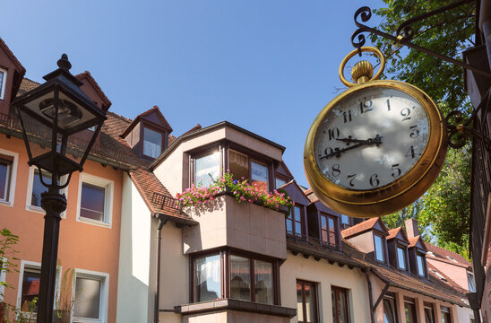 Large vintage hanging clock beside traditional residential buildings on a sunny street in Nuremberg, Germany.