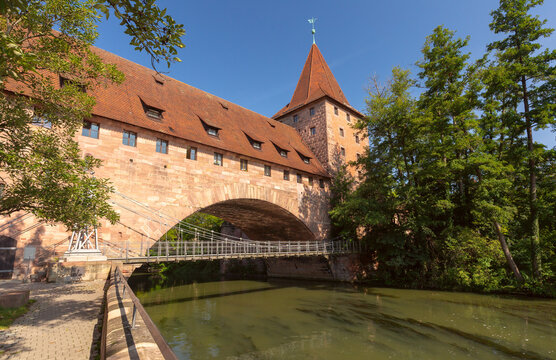 Historic stone gate with a tower beside the Pegnitz River on a sunny summer day in Nuremberg, Germany.