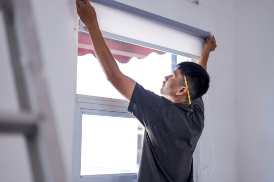 Asian Technician Installing Roller Window Blinds During Home Interior Renovation