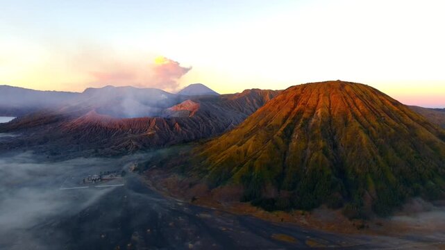 Aerial view of Mount Bromo with volcanic craters, smoke, and golden sunrise light over the caldera in Tosari, East Java, Indonesia.