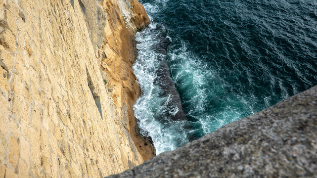 The bright blue waves of the Mediterranean Sea crash against a beige cliff off of the coast of Naples in southern Italy