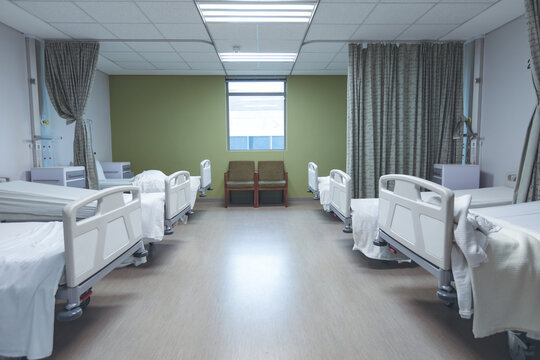 Modern hospital ward with multiple empty patient beds and medical curtains along the walls