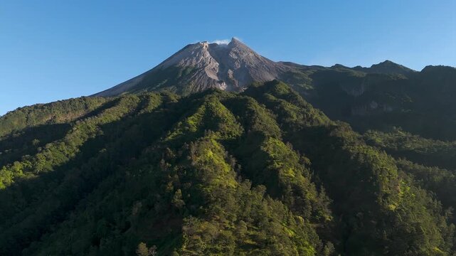 Aerial view of Mount Merapi volcano with lush green forested slopes under a clear blue sky in Cangkringan, Special Region of Yogyakarta, Indonesia.