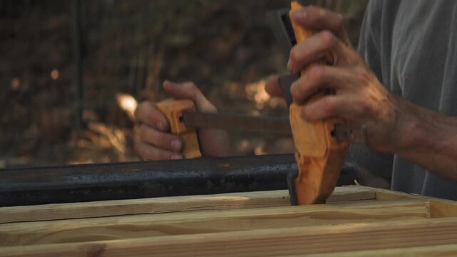 Man's hands using clamp to hold metal pipe on wooden planks outdoors.