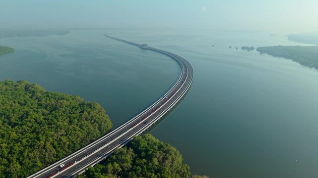 Aerial view of the Bali Mandara Toll Road stretching across the calm waters of the bay, surrounded by lush mangrove forests in Kecamatan Kuta Selatan, Bali, Indonesia.