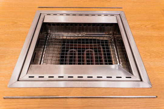 Empty stainless steel electric tabletop grill with glowing heating elements built into a wooden restaurant table