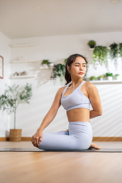 Asian woman practicing yoga in seated twist pose at home with calm focus and balanced posture