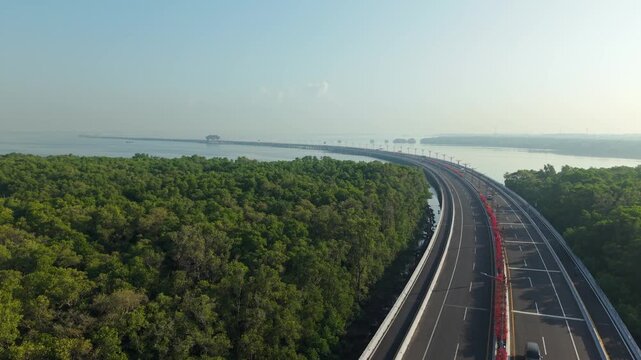 Aerial view of Bali Mandara Toll Road stretching across the sea with lush mangrove forests and clear sky in Kecamatan Kuta Selatan, Bali, Indonesia.