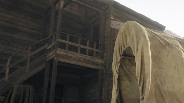 A wooden building stands next to a covered wagon in a rural area. The scene shows the architecture of the building with steps and a balcony above. The setting has a simple, natural look.