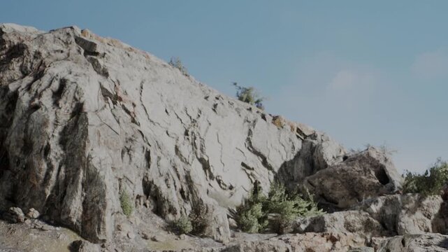 A large rocky area shows various sizes of stones and bushes. The scene is bright with clear blue sky. Sunlight illuminates the rocks during the day.