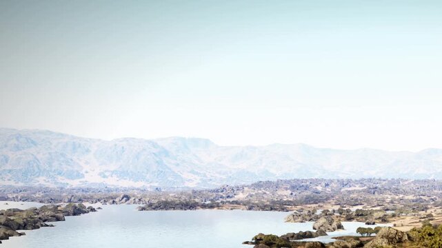 A large body of water flows through rocky terrain surrounded by mountains. This scene shows a bright sky above the calm lake during daylight hours.