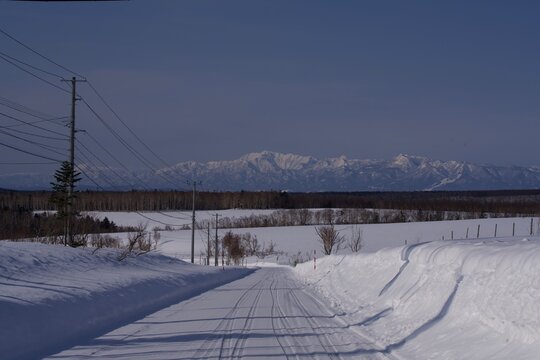 Straight snowy road leading toward a white mountain range, Hokkaido, Japan