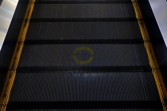 Close-up texture of black escalator steps with yellow safety edge lines in a modern building.