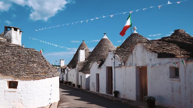 Alberobello trulli houses with traditional conical roofs and fluttering italian flags under blue sky in puglia italy.