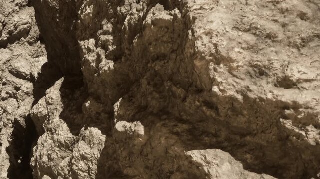 The scene shows a close up view of a rock formation in a natural setting. Sunlight highlights the texture and details of the rocks, creating interesting shadows.