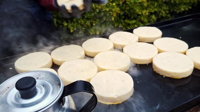 Close-up of arepa street food being prepared, with melted butter spread on grilled corn cakes on a hot grill. Sizzling sound, crispy texture and traditional Colombian food concept. 